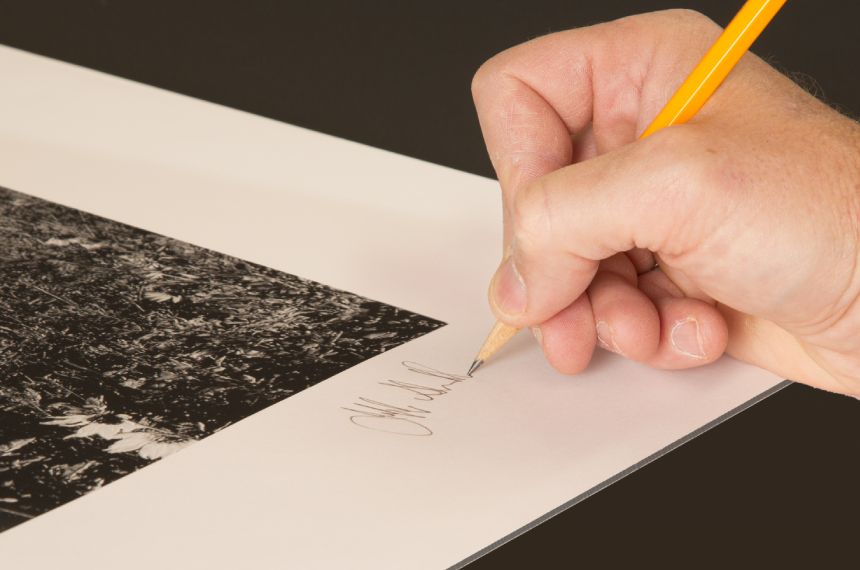 A person writing on paper with pencil.