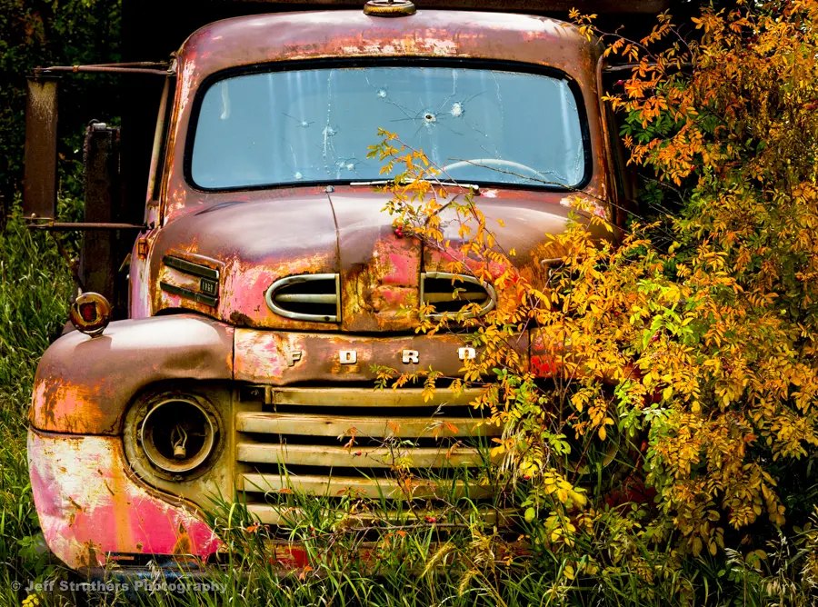 A rusty old truck is parked in the grass.